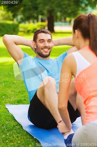 Image of smiling man doing exercises on mat outdoors