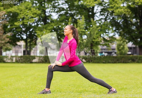 Image of smiling black woman stretching leg outdoors