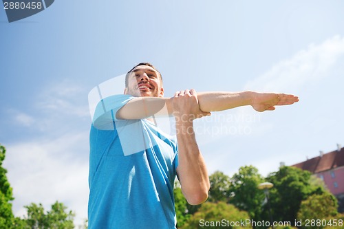 Image of smiling man stretching outdoors