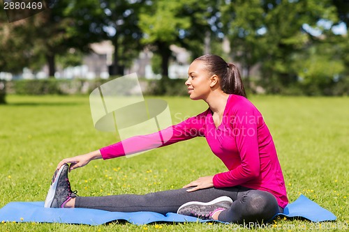 Image of smiling woman stretching leg on mat outdoors