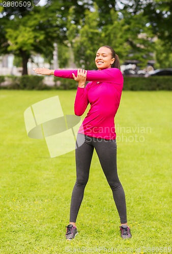 Image of smiling black woman stretching leg outdoors