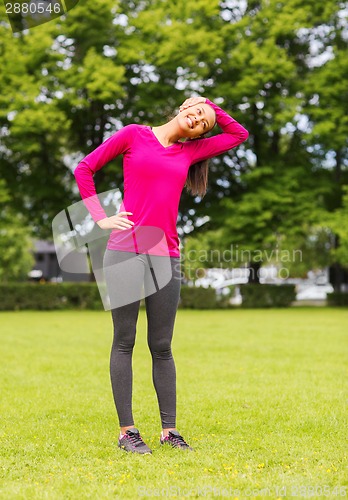 Image of smiling black woman stretching leg outdoors