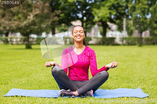 Image of smiling woman meditating on mat outdoors