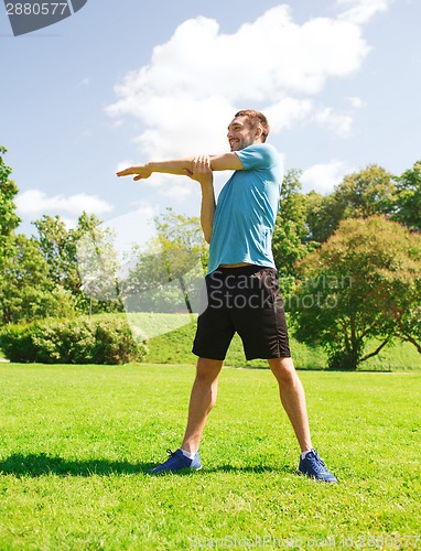 Image of smiling man stretching outdoors