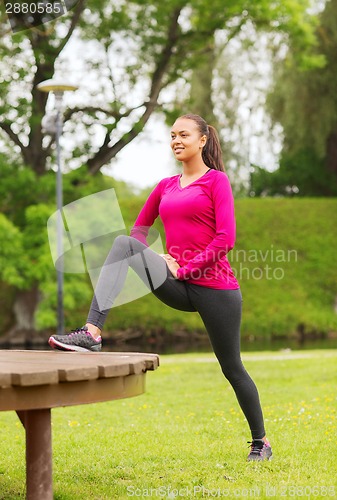 Image of smiling woman stretching on bench outdoors