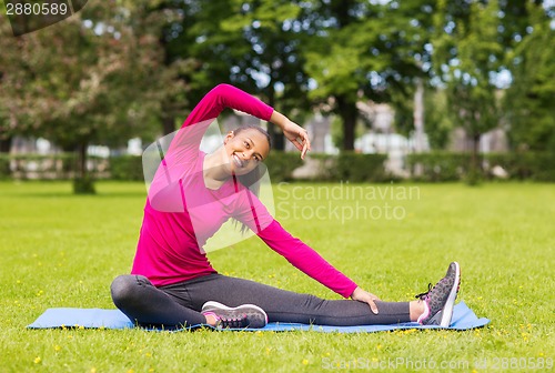Image of smiling woman stretching leg on mat outdoors