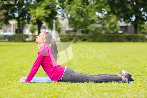 Image of smiling woman doing exercises on mat outdoors
