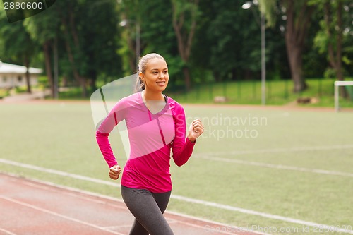 Image of smiling woman running on track outdoors