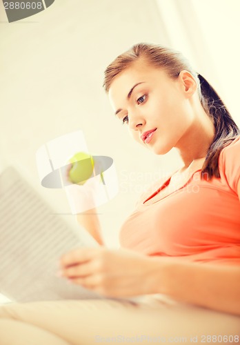 Image of woman with green apple reading newspaper at home