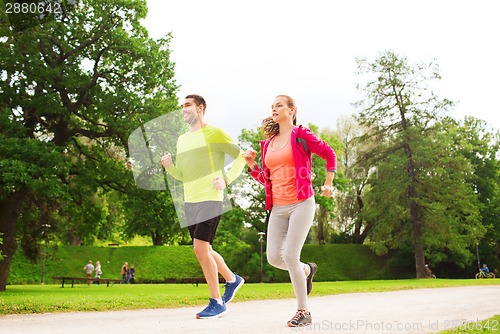 Image of smiling couple with earphones running outdoors