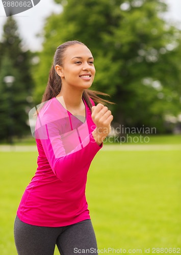 Image of smiling young woman running outdoors