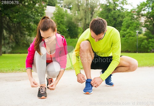 Image of smiling couple tying shoelaces outdoors