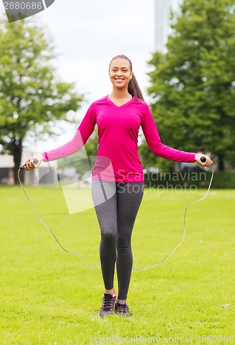 Image of smiling woman exercising with jump-rope outdoors