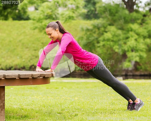 Image of smiling woman doing push-ups on bench outdoors