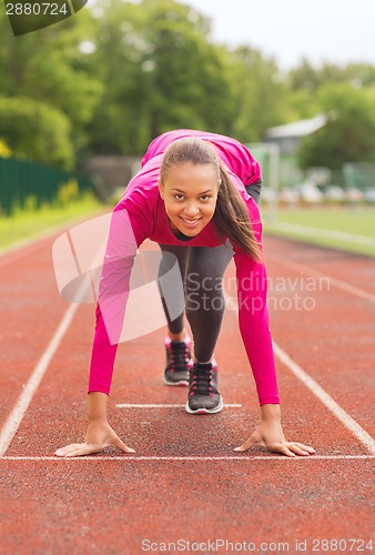Image of smiling young woman running on track outdoors