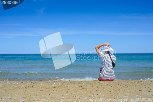 Image of Young woman sitting on beach and looking to a sea
