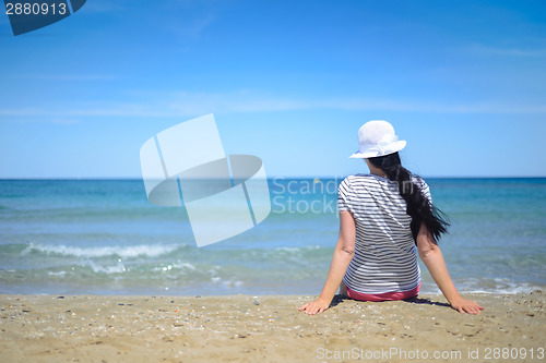 Image of Young woman sitting on sand and looking to a sea