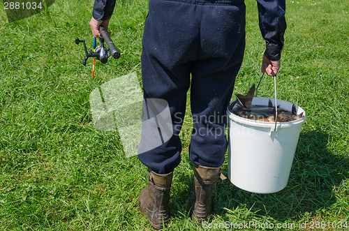 Image of weary man hold bucket full of fishes and rod 