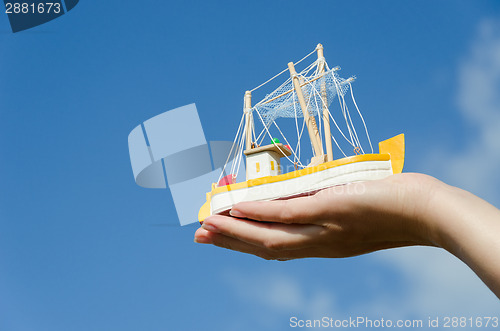 Image of wooden ship toy on palm on blue sky background 