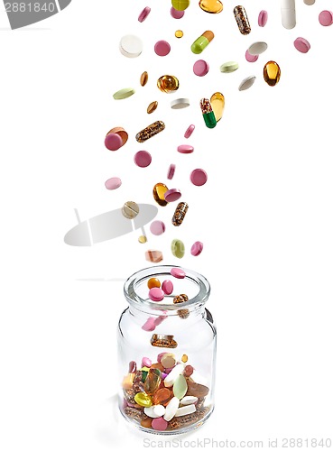 Image of various medical pills falling into glass jar