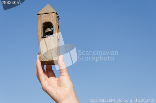 Image of hand hold belfry miniature on blue sky background 