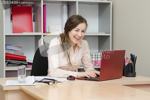 Image of Laughing girl working at laptop in office