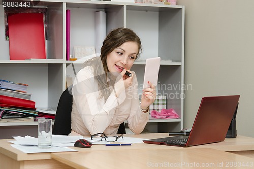 Image of Business girl paints lips with lipstick in the office