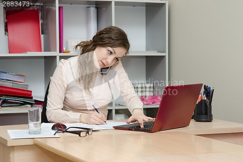 Image of Girl calling by phone and working on laptop