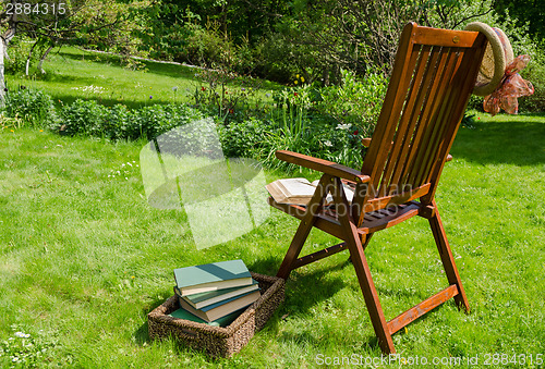 Image of wooden chair books and hat in garden 