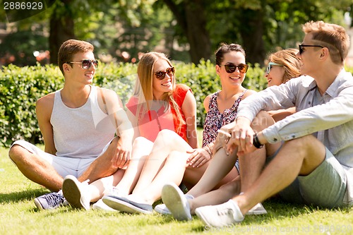 Image of group of smiling friends outdoors sitting on grass