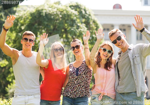 Image of group of smiling friends waving hands outdoors