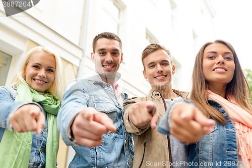 Image of group of smiling friends in city pointing finger