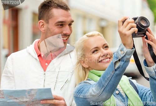 Image of smiling couple with map and photocamera in city