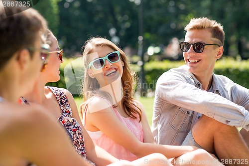 Image of group of smiling friends outdoors sitting in park