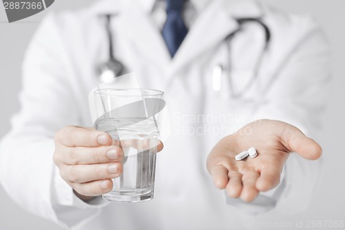 Image of doctor hands giving white pills and glass of water