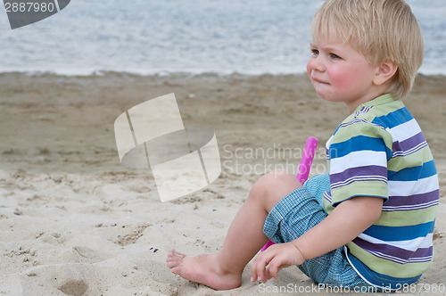 Image of Little toddler boy sitting on sand beach