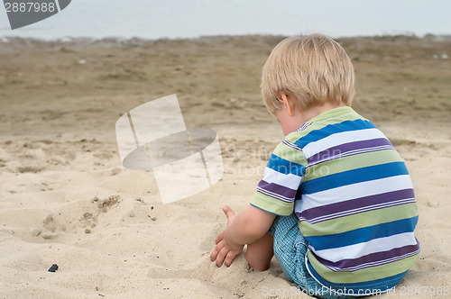 Image of Little toddler boy sitting back on sandy beach