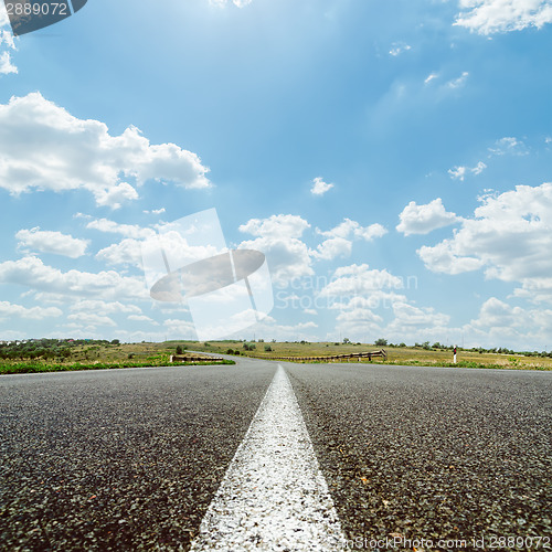 Image of white line on asphalt road under sky with sun and clouds