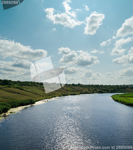 Image of light clouds in blue sky over river with reflections