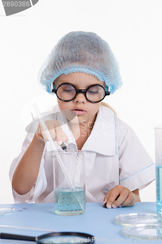 Image of Girl chemist pours reagent into the flask with liquid