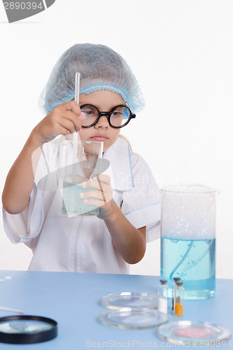 Image of Girl chemist mixes the contents of flasks