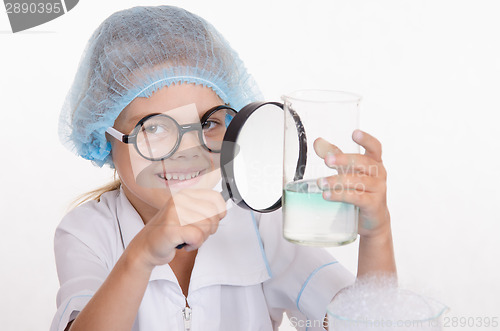 Image of Chemist examines a flask under magnifying glass