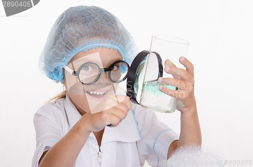 Image of Girl chemist examines flask under a magnifying glass