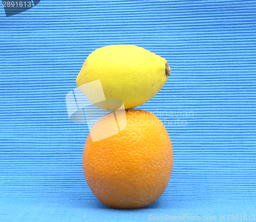 Image of A lemon lying upon an orange on a  blue background
