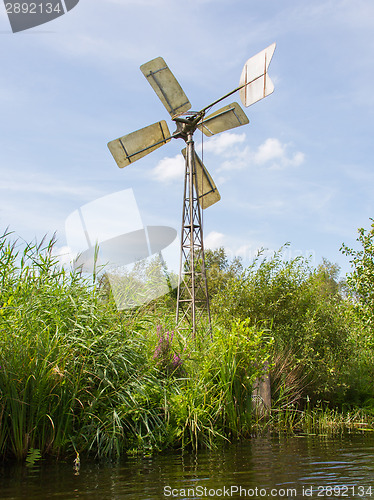 Image of Small and rusted old metal windmill at the waterside
