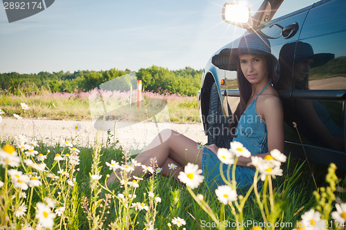 Image of Young pretty woman sitting near green car