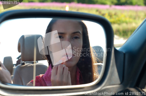 Image of Woman applying lipstick looking at car mirror