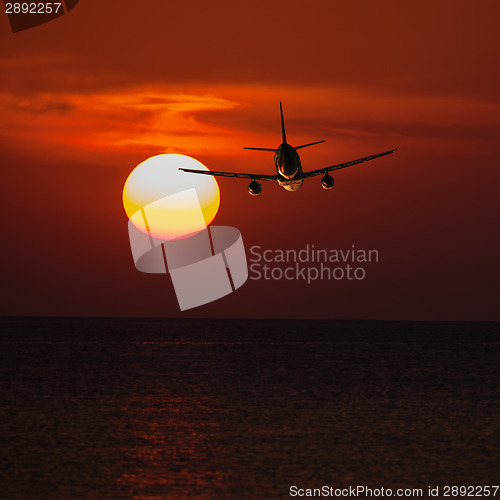 Image of Passenger plane flying at a low altitude at sunset and the sun b