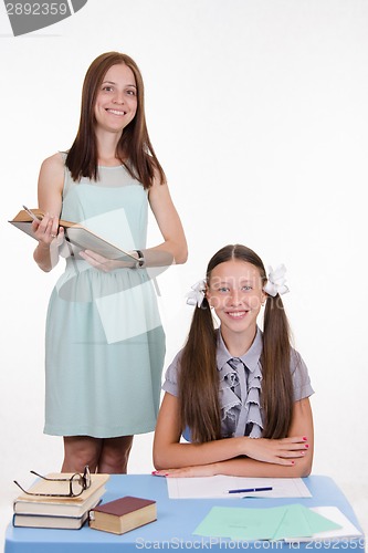 Image of Pupil at school desk, teacher standing with a book