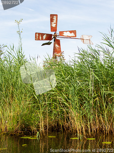 Image of Small and rusted old metal windmill at the waterside